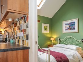 A kitchen area with wooden cabinets and a tiled backsplash next to a bedroom with a bed and green walls at The Barn in Lifton