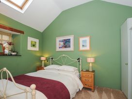 A bedroom with a bed with white bedding and a purple throw two wooden bedside tables with lamps and pictures on a green wall at The Barn in Lifton