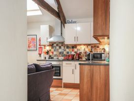 A kitchen with wooden beams white cabinets and tiled backsplash with a black countertop and appliances and a sofa in foreground at The Barn in Lifton