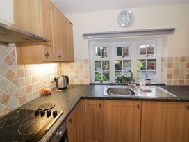 A kitchen with wooden cabinets a tiled backsplash a sink under a window and a stovetop at Rooster in Stourport-On-Severn