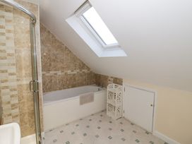A bathroom with a bathtub under a skylight a shower enclosure and a small shelving unit at Rooster in Stourport-On-Severn