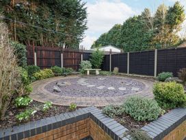 A backyard garden with a circular stone patio a stone bench and plants at Rooster in Stourport-On-Severn