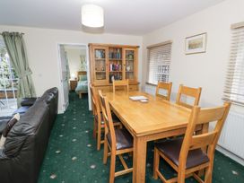 A dining area with a wooden table and six chairs next to a glass-front cabinet and a black leather sofa at Hen and Chickens in Stourport-On-Severn