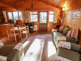 A wooden cabin living room with green upholstered sofas a round wooden dining table and kitchen appliances at Goldcrest in Withern near Alford