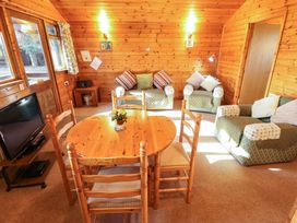 A wooden dining table with four chairs a television and three armchairs in a wooden cabin living room at Goldcrest in Withern near Alford