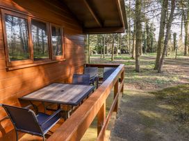 A wooden balcony with a square table and four chairs overlooking a wooded area at Goldcrest in Withern near Alford