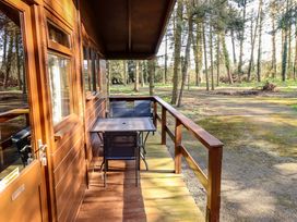 A wooden porch with a table and four chairs overlooking a wooded area at Goldcrest in Withern near Alford