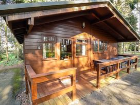 A wooden cabin with a porch and outdoor table and chairs set among trees at Goldcrest in Withern near Alford