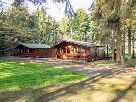 Two wooden cabins with patios surrounded by trees and grass at Goldcrest in Withern near Alford
