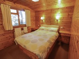 A bedroom with a bed placed against wooden walls under two wall lamps and a window with curtains at Goldcrest in Withern near Alford