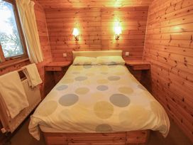 A bedroom with a double bed, wooden walls, two bedside shelves, two wall lamps, a window with curtains and towels on a radiator at Goldcrest in Withern near Alford