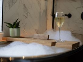 A bathroom with a bathtub, wooden tray, plant and glass at Hilltop Cottage in Conwy