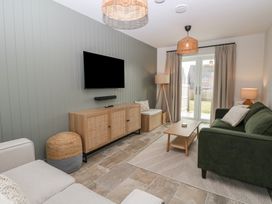 A living room with a green sofa a beige armchair wooden cabinet and a wall-mounted television at The Hideaway Cromer in Northrepps near Overstrand