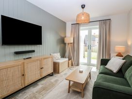 A living room with a green sofa a wooden coffee table a television on the wall and glass doors at The Hideaway Cromer in Northrepps near Overstrand