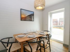 A dining area with a wooden table set with plates and glasses and six black chairs near a window at The Hideaway Cromer in Northrepps near Overstrand