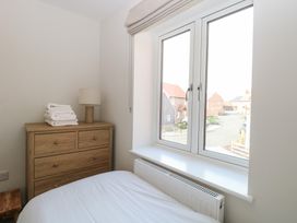 A bedroom with a wooden dresser holding a lamp and folded towels next to a window at The Hideaway Cromer in Northrepps near Overstrand