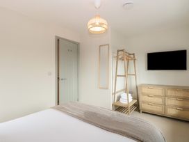A bedroom with a bed a wooden clothing rack with hangers and folded towels a wooden dresser and a wall-mounted TV at The Hideaway Cromer in Northrepps near Overstrand
