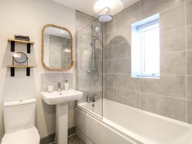 A bathroom with a bathtub shower combination a pedestal sink a toilet a mirror and shelves at The Hideaway Cromer in Northrepps near Overstrand