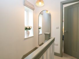 A hallway with a window and flowers on the sill a mirror on the wall and a partially open door at The Hideaway Cromer in Northrepps near Overstrand