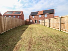 A backyard with grass and wooden fences surrounding two brick houses with solar panels on the roofs at The Hideaway Cromer in Northrepps near Overstrand