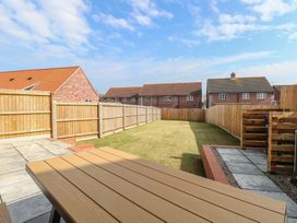 A backyard with grass lawn wooden fence and patio area at The Hideaway Cromer in Northrepps near Overstrand
