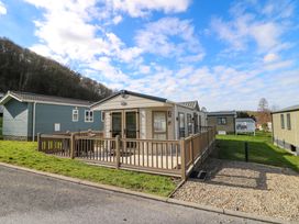 A mobile home with a wooden deck and railing on a grassy lot at 98 The Heron in New Quay
