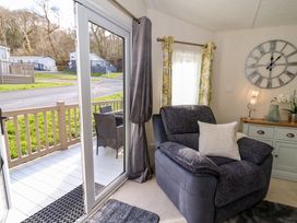 A living room with a large armchair a sideboard with a clock on the wall and sliding glass doors leading to a patio at 98 The Heron in New Quay