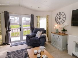 A living room with an armchair next to glass doors and a cabinet with a clock on the wall at 98 The Heron in New Quay