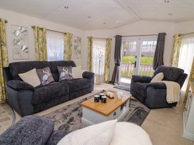 A living room with dark sofas, a wooden coffee table with mugs and a teapot, floral curtains, and glass doors at 98 The Heron in New Quay