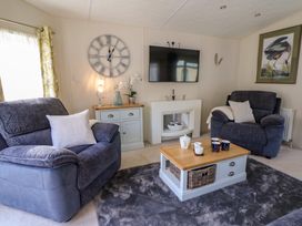 A living room with two dark armchairs a coffee table with mugs and teapot a wall clock and a mounted TV at 98 The Heron in New Quay