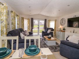 A living room with grey sofas a coffee table and dining table with blue plates at 98 The Heron in New Quay