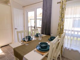 A dining area with a set table for four near a window and a glass door at 98 The Heron in New Quay