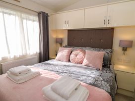 A bedroom with a double bed with pink and grey bedding and pillows bedside tables with lamps and cabinets above the bed at 98 The Heron in New Quay