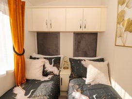 A bedroom with two single beds with patterned bedding and orange curtains at 98 The Heron in New Quay