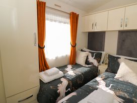 A bedroom with two single beds with bird-patterned bedding and orange curtains at 98 The Heron in New Quay