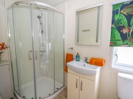 A bathroom with a corner shower enclosure a sink with orange towels and a mirror at 98 The Heron in New Quay