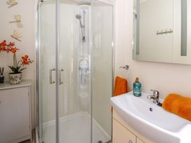 A bathroom with a corner shower enclosure a sink with orange towels and a soap dispenser and a cabinet with a flower pot at 98 The Heron in New Quay