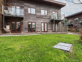 A wooden two story building with balconies chairs and glass doors in front of a grass lawn at Treveglos in Porthtowan
