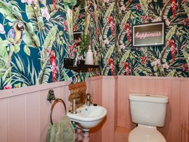 A bathroom with a toilet and sink with tropical bird wallpaper and pink paneling at Treveglos in Porthtowan