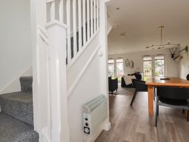 A dining area with a wooden table and black chairs next to a living room with sofas and windows at Treveglos in Porthtowan