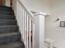 A staircase with grey carpet and white banister with a wall lamp and framed art on the wall at Treveglos in Porthtowan