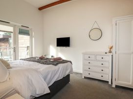A bedroom with a bed and white linens a dresser with a mirror on the wall and a TV mounted on the wall at Treveglos in Porthtowan