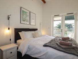 A bedroom with a made bed white nightstand hanging bedside lamp and framed pictures above at Treveglos in Porthtowan