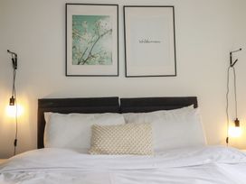 A bed with white bedding and pillows with two framed pictures above and two hanging light bulbs at Treveglos in Porthtowan
