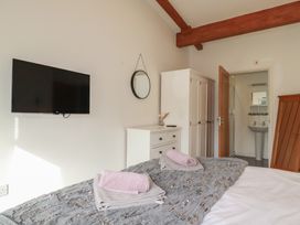 A bedroom with a bed towels on a blanket a wall-mounted TV a mirror a white dresser a white wardrobe and an open door leading to a bathroom at Treveglos in Porthtowan
