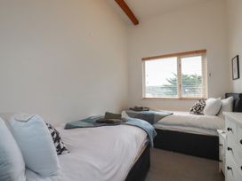 A bedroom with two single beds near a window with blinds and a white chest of drawers at Treveglos in Porthtowan