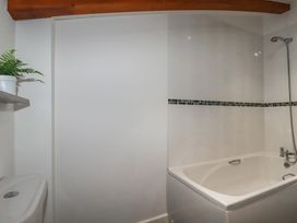 A bathroom with a white bathtub showerhead toilet wooden ceiling beam and a plant on a wall shelf at Treveglos in Porthtowan