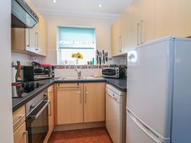 A kitchen with wooden cabinets black countertop a white refrigerator a dishwasher a window with a blue blind and a vase with sunflowers at No 108 Waterside in Corton