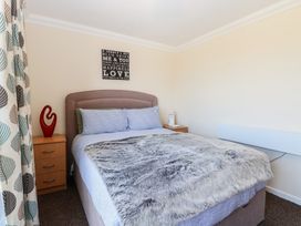 A bedroom with a double bed a fur blanket wooden bedside tables and curtains with leaf patterns at No 108 Waterside in Corton