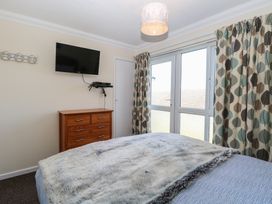 A bedroom with a bed covered in a fur throw a wooden chest of drawers a wall-mounted TV double glass doors with patterned curtains at No 108 Waterside in Corton